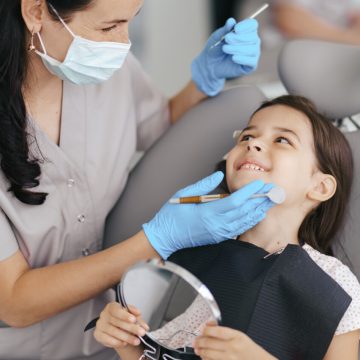 Cute little girl sitting on a modern dental chair and having dental consultation with dentist